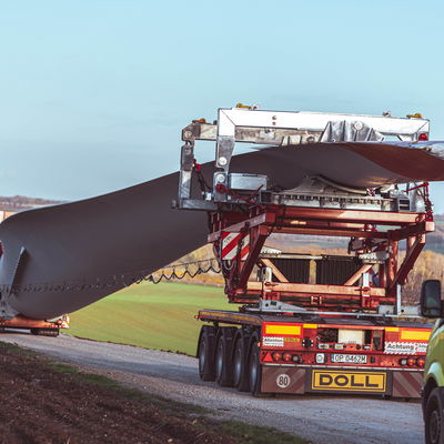 Schwertransport eines Windflügels auf einem spezialisierten LKW-Anhänger von DOLL auf einer Landstraße.