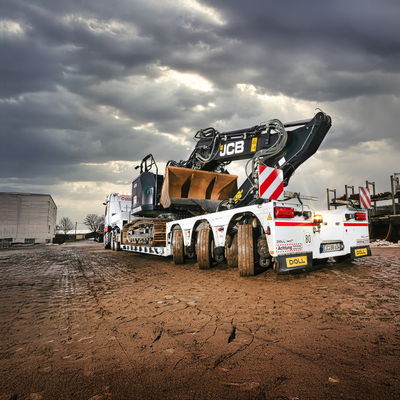 Pelleteuse stationnée sur une remorque surbaissée pour transport lourd sous un ciel dramatique.