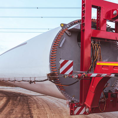 Nahaufnahme eines Schwertransports mit Windturbinenmast, gesichert mit rotem Spezialhalter auf einem DOLL-Nachläufer.