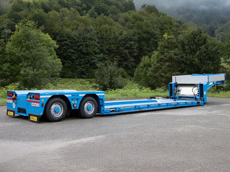 Blue low-loader trailer with hydraulic ramps, designed for transporting heavy equipment, parked on a roadside.