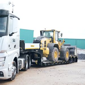 Truck with DOLL low-loader trailer, on which a construction site vehicle is loaded, drives around a bend