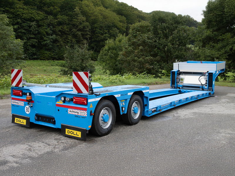 Blue low-loader trailer with hydraulic ramps, designed for transporting heavy equipment, parked on a roadside.