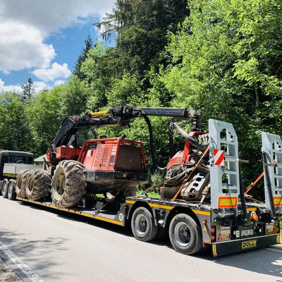 Tracteur lourd sécurisé sur une remorque plate pour transport sur une route forestière sous un ciel ensoleillé.