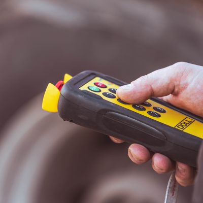 Close-up of a hand holding a yellow-black remote control by DOLL for operating a heavy transport vehicle.