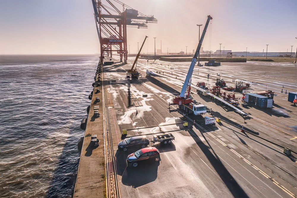 Schwertransport von Windradflügeln mit Kränen am Hafen bei Sonnenuntergang